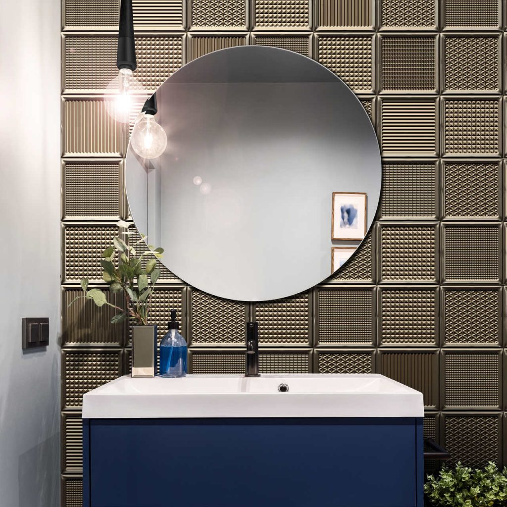 Blauer Waschbeckenunterschrank im Kontrast zu braunen Fliesen in Glasoptik. Moderner, runder Spiegel hellt die Farbe auf.